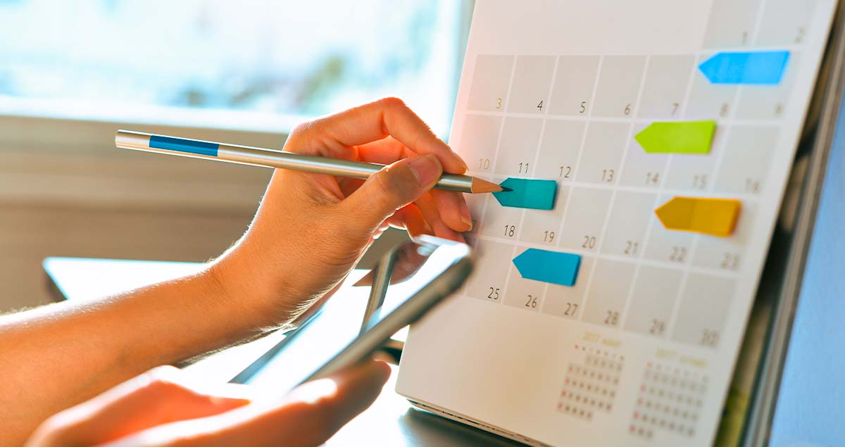 Mão escrevendo em calendário com datas marcadas