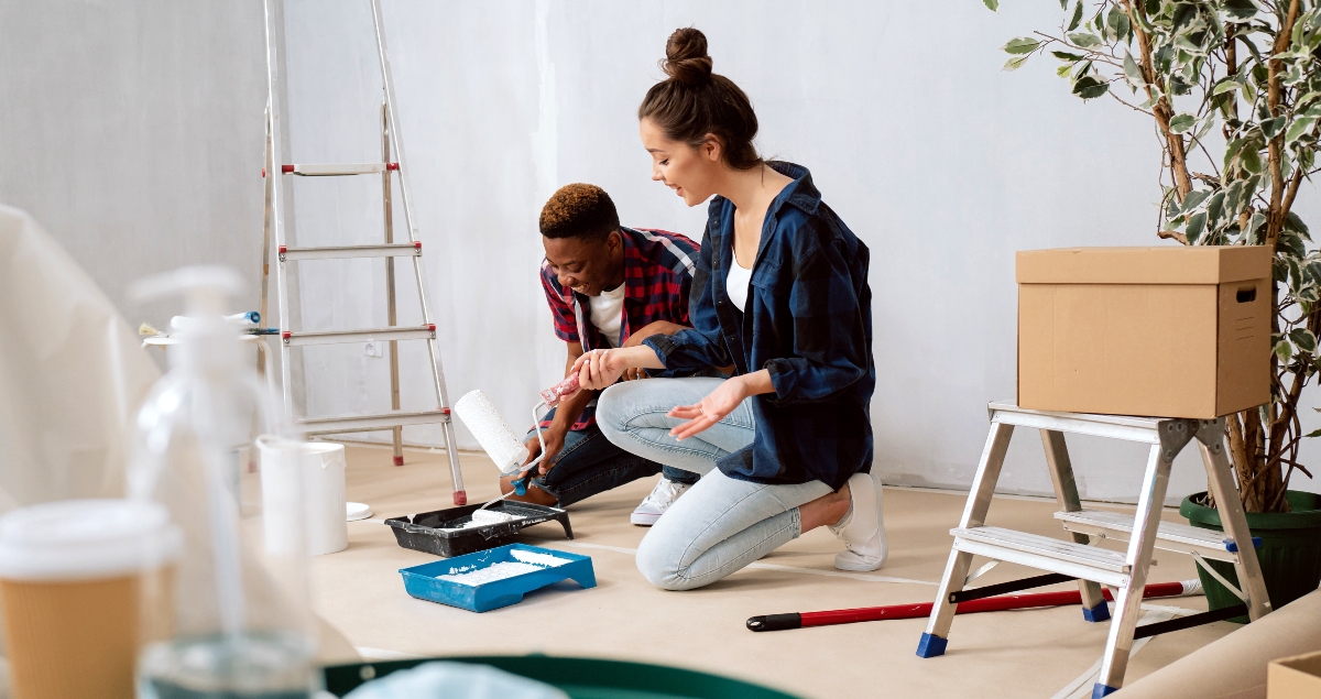 Duas pessoas pintando sala de apartamento com caixas e itens ao redor
